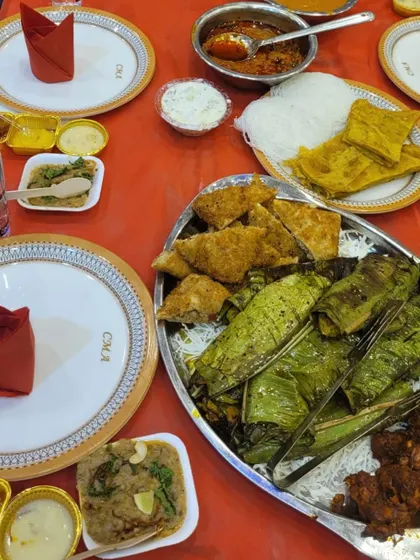 A perfectly set table ready for guests. It features a platter of fish cooked in banana leaves, along with various side dishes and condiments, showcasing a complete meal setup.