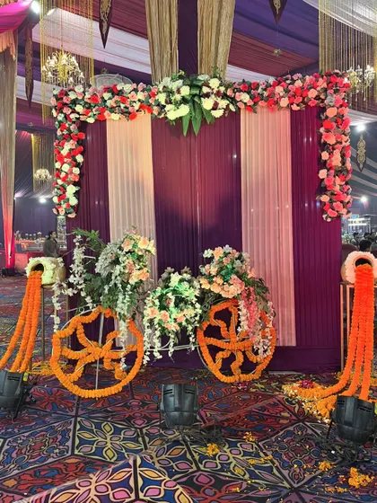 A whimsical floral bicycle prop, perfect for a Mehndi or garden party, decorated with marigold garlands and set against a purple and white striped backdrop.