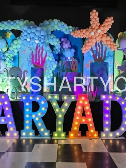 A vibrant underwater stage with a balloon-sculpted starfish and octopus, a mermaid tail prop, and rainbow-colored marquee letters.