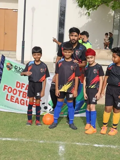 A young team poses with their coach in front of the DFA League banner.