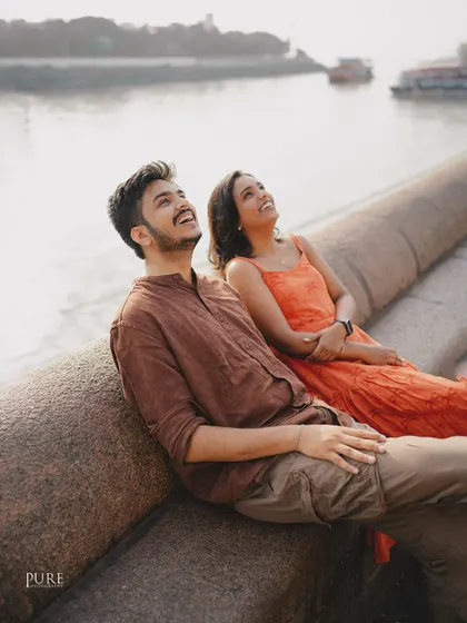 Pure joy captured in a candid moment. Nikit and Anusha look up at the sky, laughing together by the water, showing the simple happiness that defines their relationship.