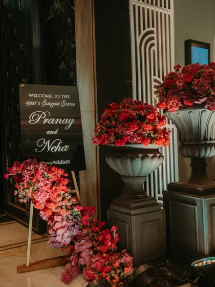 The welcome signage for the "1920's Sangeet Soiree," flanked by dramatic red floral arrangements, setting the tone for a night of vintage glamour.