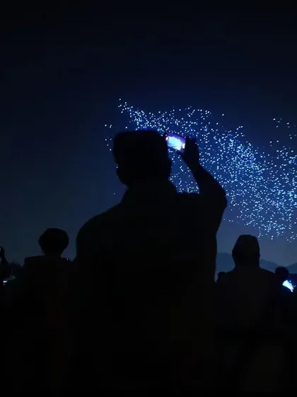 Silhouetted against the night sky, a crowd captures our drone formations on their phones. This image perfectly illustrates the shared experience and viral nature of our shows.