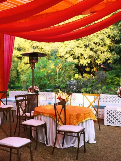 An outdoor seating area for a Mehendi function, with bright red and orange drapes creating a warm and festive canopy.