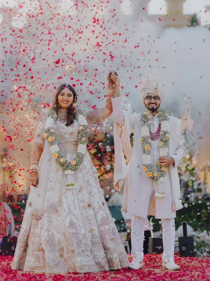 A beautiful portrait of the newly married couple after their Varmala, holding hands and celebrating their union under a rain of petals.
