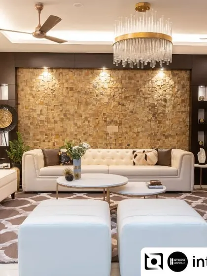 This luxurious living room features a stunning accent wall with natural stone cladding. The neutral tufted sofas, elegant chandelier, and marble coffee tables come together to create a space that is both grand and welcoming.