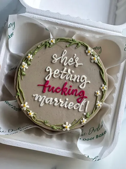 A cheeky and fun mini cake for a bride-to-be. The message "she's getting fucking married!" is framed by a delicate, hand-piped floral wreath. It's the perfect cake for a bachelorette party.