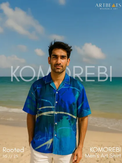 The Komorebi Men's Art Shirt, seen here against a beach backdrop. This luxe sustainable silk shirt draws from the Japanese philosophy of "Komorebi," or sunlight filtering through trees.