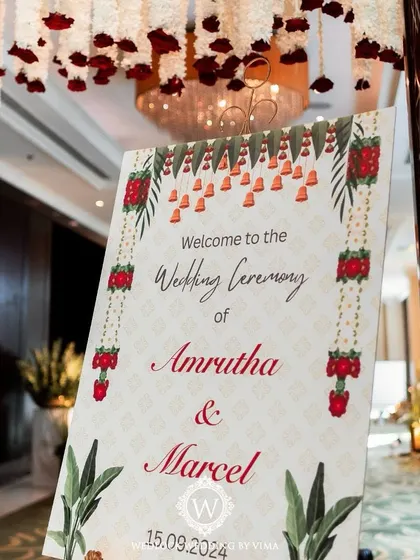 A custom welcome sign for a traditional red and white wedding. The design incorporates classic Indian motifs like bells and floral garlands, perfectly matching the theme.