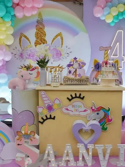 A unicorn-themed dessert bar setup with a large backdrop, rainbow balloon arch, and themed props.