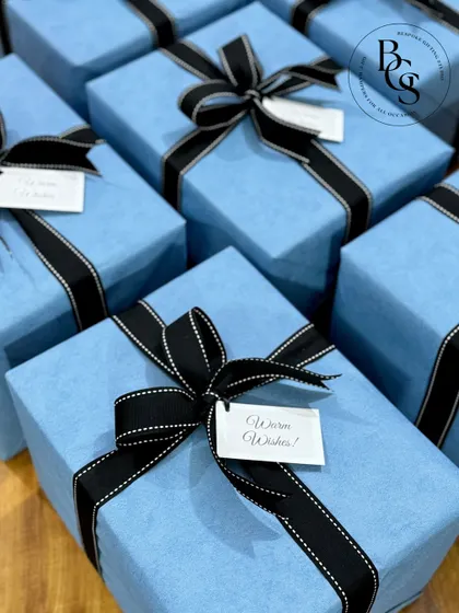 A set of impeccably wrapped gifts in a serene light blue, contrasted with bold black grosgrain ribbons. This classic and chic presentation is perfect for corporate events, formal celebrations, or any occasion that calls for timeless elegance.