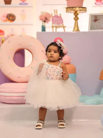 The birthday girl looking adorable in her custom dress, standing in front of giant donut and macaron props at her Candyland party.