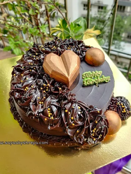 This double chocolate ganache cake is decorated with intricate piping and topped with a geometric chocolate heart and golden chocolate spheres for a modern, luxurious finish.