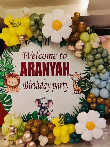 Welcome your guests in style with a themed entrance. For this jungle safari party, I designed a large circular welcome sign featuring cute animals, framed by a custom balloon garland in jungle colors with tropical leaf accents.
