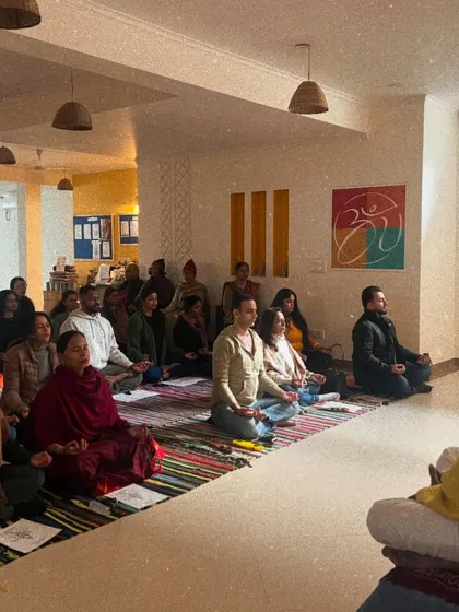 I guide a large group through meditation during a special satsang. My role is to hold the space and offer guidance, allowing each person to connect with their own inner stillness.