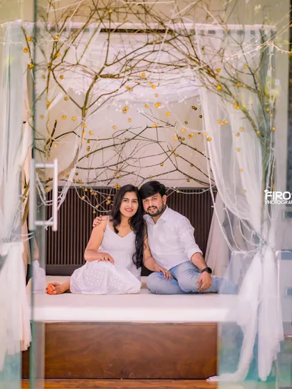 A serene portrait of a couple in a romantic indoor setting, surrounded by fairy lights and delicate white curtains. The all-white theme adds to the dreamy, ethereal feel.