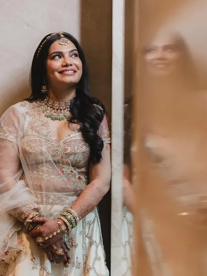 A candid moment of joy. The bride's reflection is caught in the background, showing her happiness with the flawless and long-lasting makeup.
