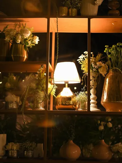 A warm, inviting detail shot of a lamp on a shelf, surrounded by small floral arrangements. This creates a cozy, home-like feeling even in a large event space.