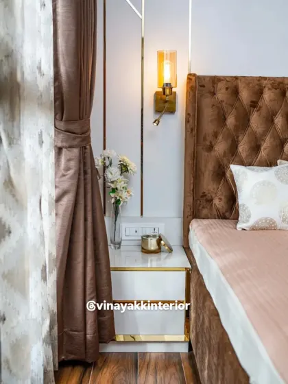 It's all in the details. This close-up shows the elegant bedside setup, with a sleek white and gold nightstand, a stylish wall sconce for reading, and the rich, diamond-tufted pattern of the headboard.
