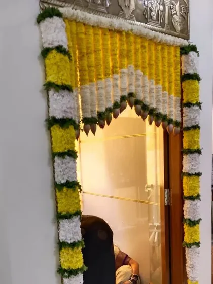 A pooja door decorated with white and yellow flowers, with hanging lotus buds. This is a clean and elegant design for festivals like Varamahalakshmi pooja.