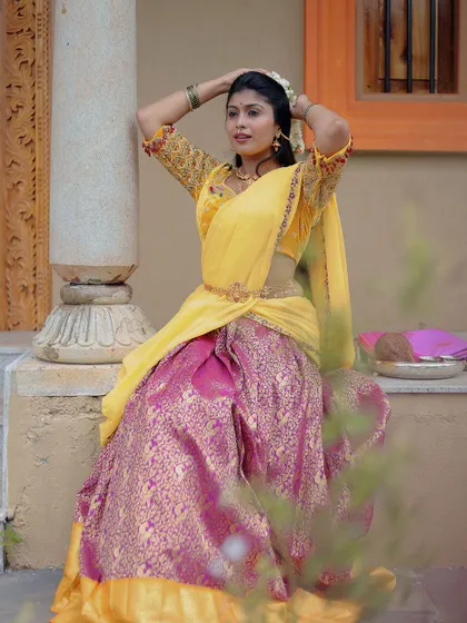 A seated pose in the yellow and pink brocade half saree, highlighting the beautiful fall of the lehenga.