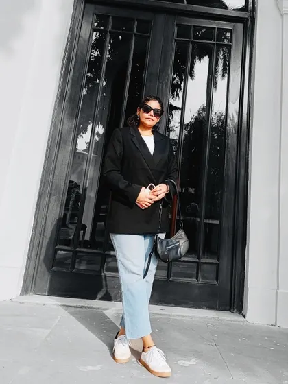 A minimalist and chic look featuring a black oversized blazer, a simple white tee, and light-wash jeans. This full-length shot showcases a classic, effortless street-style outfit.
