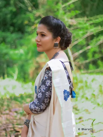 A profile shot showcasing the intricate hairstyle and the elegant drape of the saree in a natural park setting.