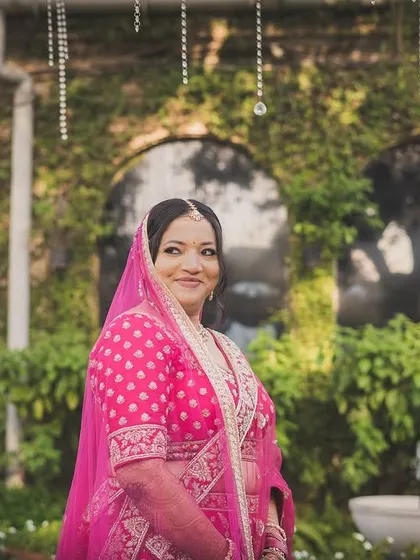 A happy portrait of Nerissa in her vibrant pink lehenga, set against a lush green backdrop.