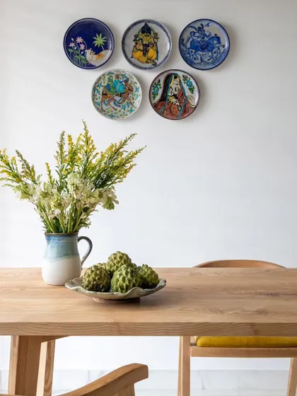 A close-up on the curated decor, featuring a collection of artistic ceramic plates on the wall. The fresh flowers on the table add a touch of natural beauty to this thoughtfully designed dining space.