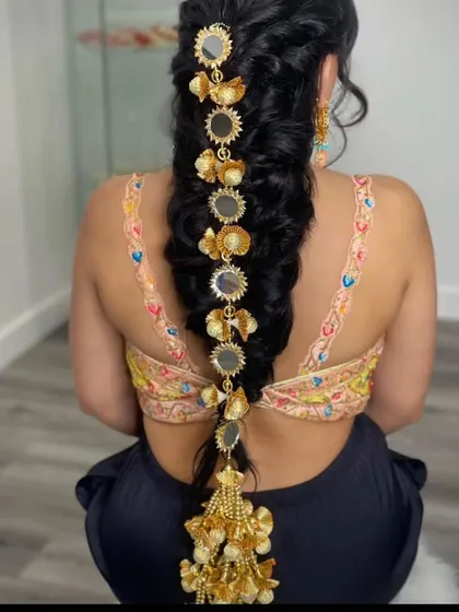 A model showing how to style a 'prandi' with mirror work and golden tassels on a long braid. This is a popular accessory for Mehendi and Sangeet functions.