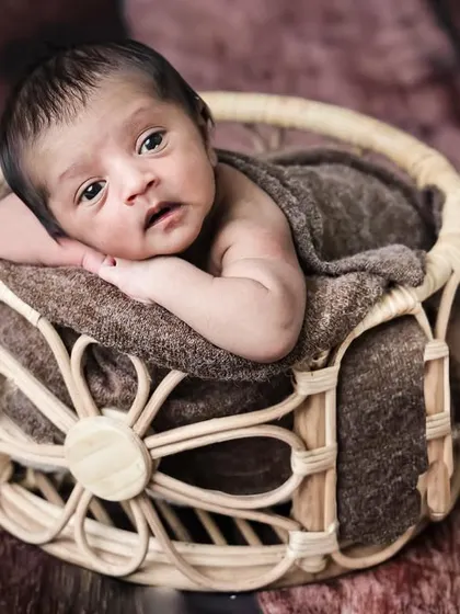 An awake and alert newborn looking directly at the camera from a wicker basket. We are skilled at capturing these engaging moments.