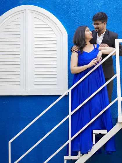 A stylish pre-wedding photo against a vibrant blue wall. The contrast of the blue dress and the background makes for a striking image.