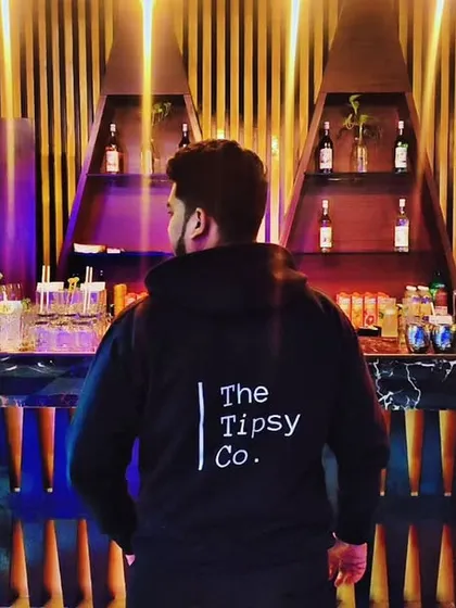 A team member proudly wearing The Tipsy Co. jacket, looking over a beautifully lit bar. This shot represents our brand identity and the world of experiences we create.