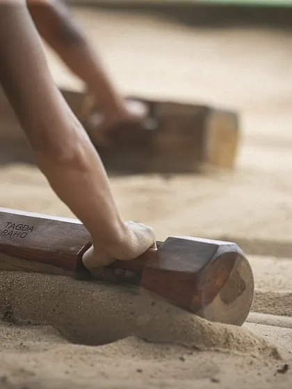 A close-up of hands gripping a Samtola in the sand. This image highlights the tactile, grounding experience of our training, where you connect directly with the earth and the equipment.