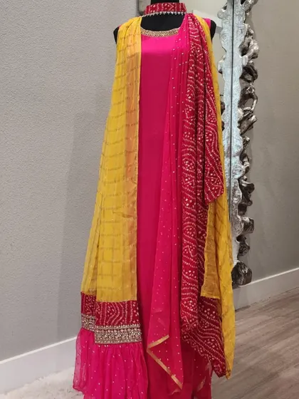 A stunning fusion gown in bright pink and yellow. This piece features a ruffled skirt, an attached Bandhani-print dupatta, and an embellished border, combining several beautiful elements into one look.