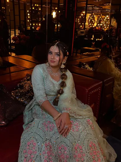 A full-length seated portrait showing the beautiful flow of the light blue lehenga. The bubble braid adds a touch of modern whimsy to the traditional attire.