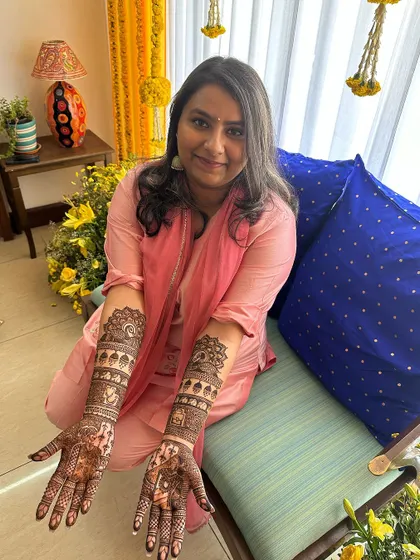 A smiling bride showing her full-arm portrait mehndi.