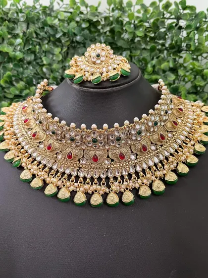 A full view of a rental choker with red and green stones, perfect for a classic bridal look. The matching maang tikka is also visible.