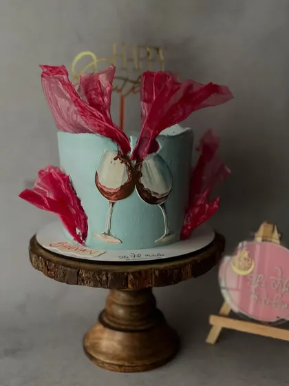 A hand-painted cake featuring two clinking wine glasses. The abstract red sails are made from edible rice paper, adding a unique texture and flair.
