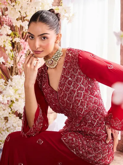 A model in a rich red embroidered outfit. The makeup is warm and defined, with a focus on the eyes and a perfectly sculpted complexion to match the regal feel of the garment.