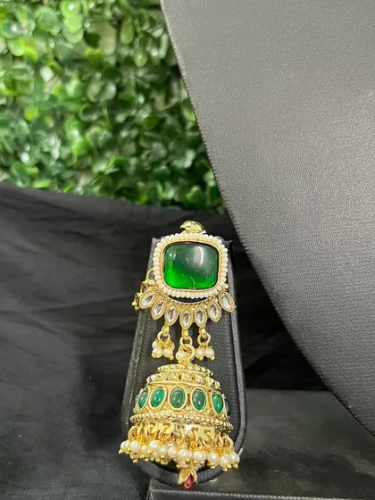 A statement earring from a rental set, featuring a large square green stone and a jhumka drop with green enamel.