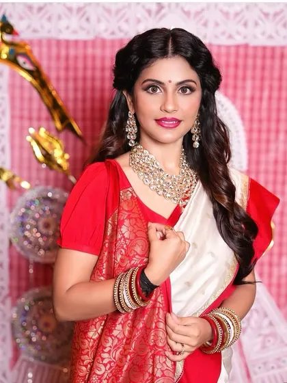 A festive Bengali look for a special occasion. The makeup features a bright lip and defined eyes, complementing the traditional red and white saree.