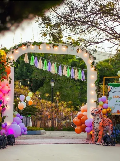 A grand entrance to a wild jungle-themed second birthday party. Guests are welcomed by an arch decorated with balloons and tassels, flanked by colorful animal statues like a deer and a leopard.