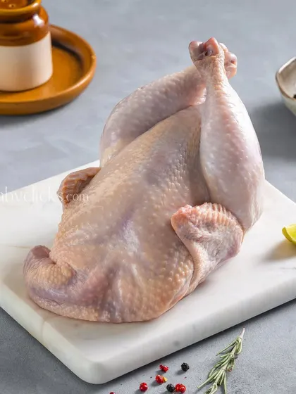 A whole raw chicken, cleaned and ready for cooking, presented on a marble slab with simple seasoning.
