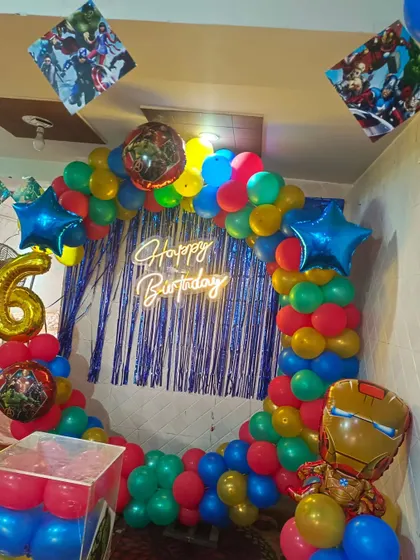 An action-packed Avengers theme for a 6th birthday. This decoration includes a colorful balloon ring, character foil balloons like Iron Man and Hulk, and a blue shimmer curtain.