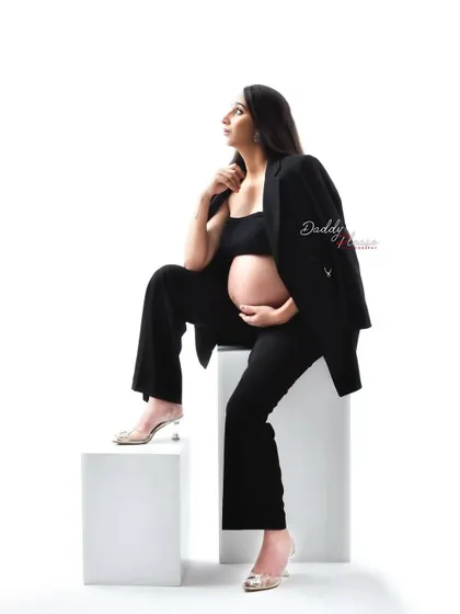 A full-body shot of the modern pantsuit look. The mom-to-be is posed on white blocks, showcasing a confident and contemporary approach to maternity photography.
