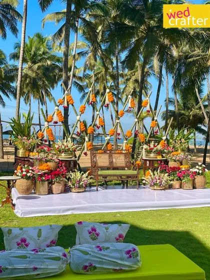 A fusion Haldi ceremony with a Malabari twist. This beachside setup features a backdrop of bamboo and marigolds, surrounded by colorful floral arrangements in earthen pots, blending tradition with a relaxed coastal vibe.