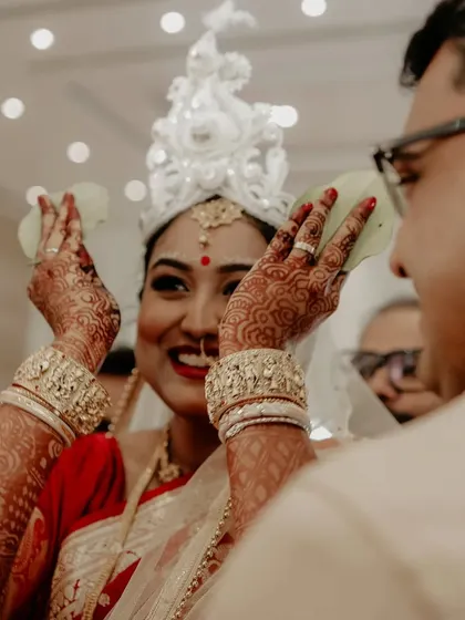 The bride reveals her face from behind the betel leaves, a key emotional moment in a Bengali wedding.