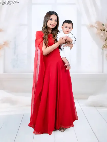 A full-length portrait of a mother in a flowing red dress holding her baby. The bright, airy background adds to the elegance of the shot.