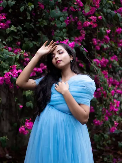 This pose highlights the delicate sleeves and neckline of the blue maternity gown, set against a vibrant floral background.